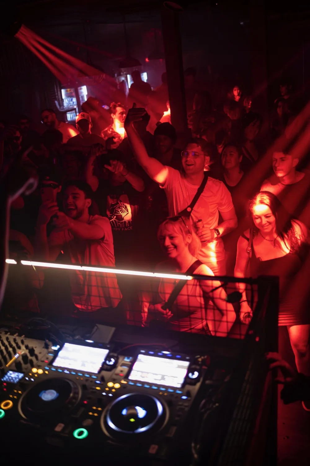 Dancers crowd the DJ booth under red light.