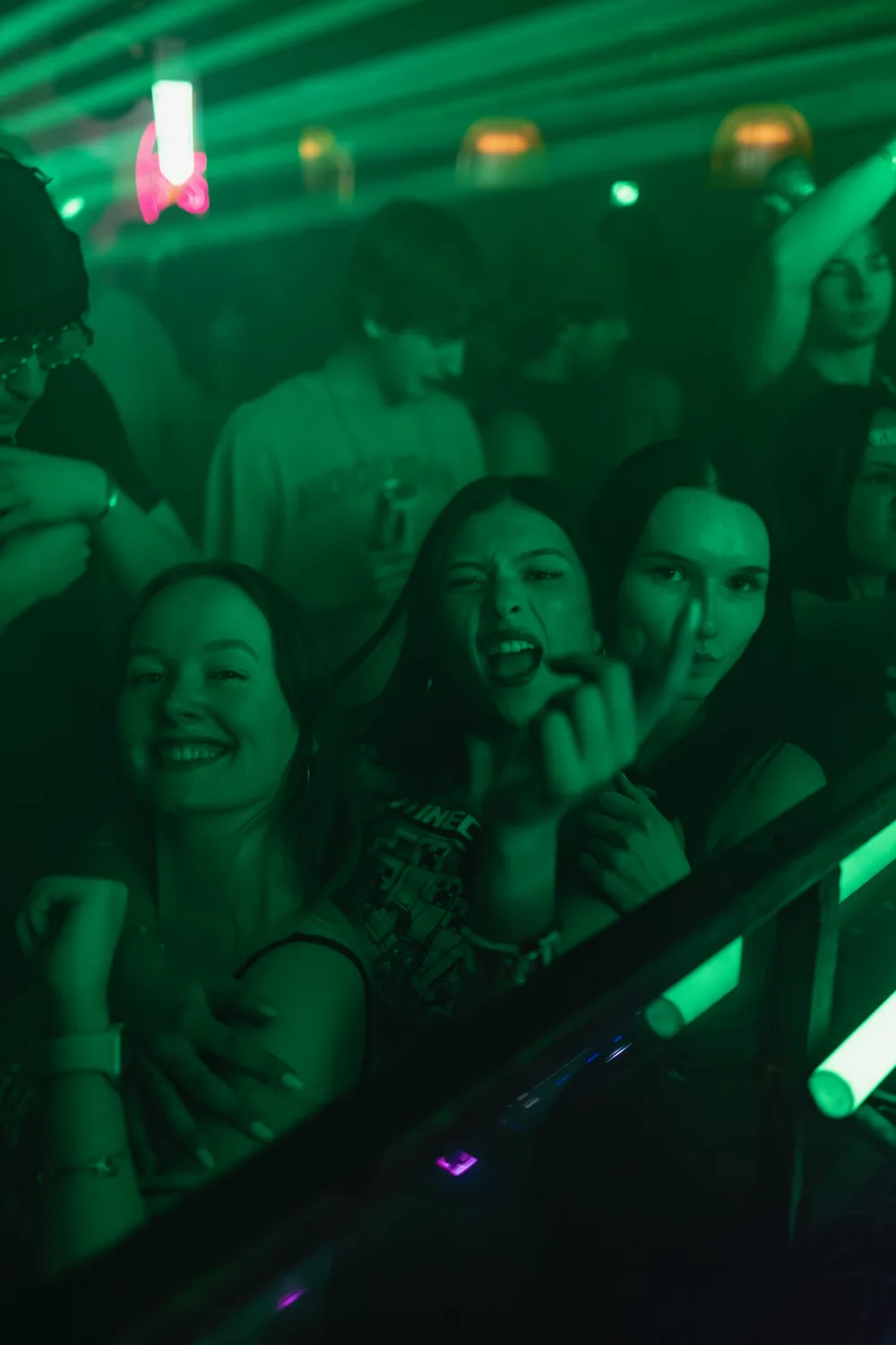 Three guests lean toward the camera beneath green club lighting.